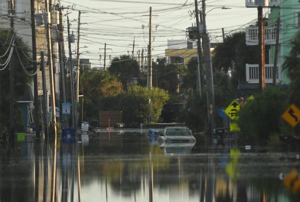 Residents observing standing flood waters around Carolina Beach Lake area, with a car driving through the flooded street.