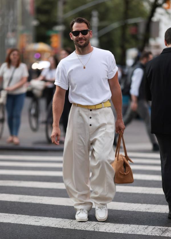 Simon Porte Jacquemus wearing black Wayfarer sunglasses, gold necklace, oversized white t-shirt, yellow braided belt, cream-white pleated pants and white boat shoes at New York Fashion Week 2024