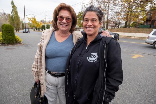 Two women smiling in a parking lot, one with the arm around the other. 