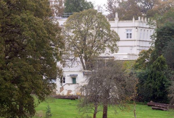 Prince Andrew driving through the gates of his deteriorating Royal Lodge in a Range Rover, with visible cracks and mould on the mansion.