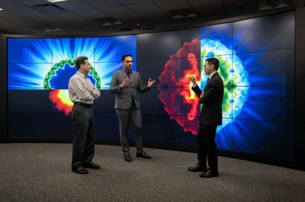 Three men stand in front of a giant screen discussing the AI and fusion research visualizations on display.