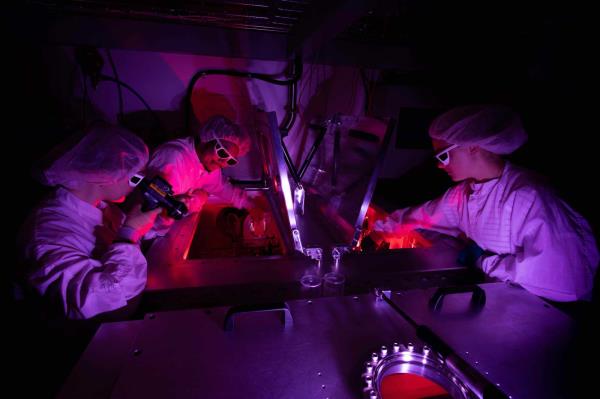 Students in a dark room and safety gear lit up with purple and red lights while co<em></em>nducting research at the University of Rochester Laboratory for Laser Energetics.