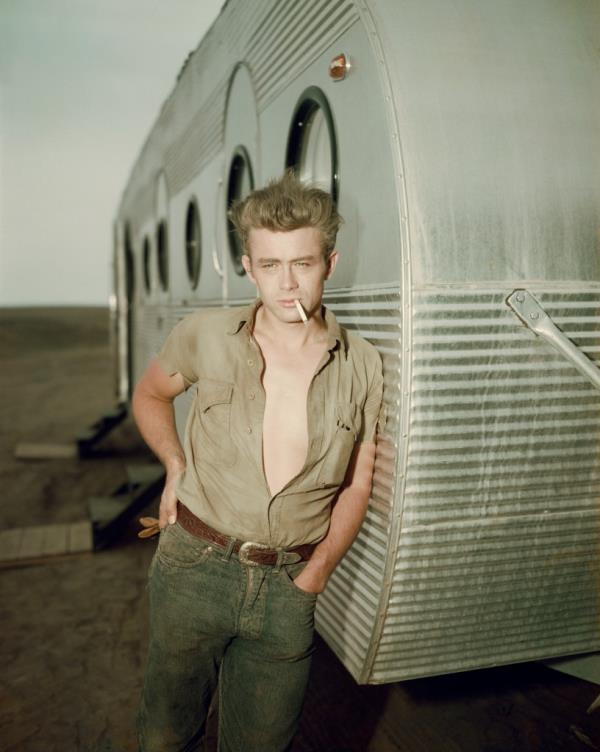 James Dean (1931 - 1955) leaning against a dressing room trailer with his shirt open to the waist while smoking a cigarette on the set of director George Stevens's film, "Giant," in which he starred. 