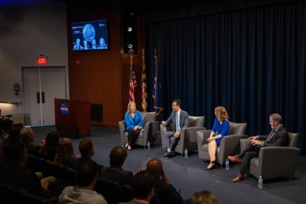 four people sit in gray chairs at the front of a crowded auditorium